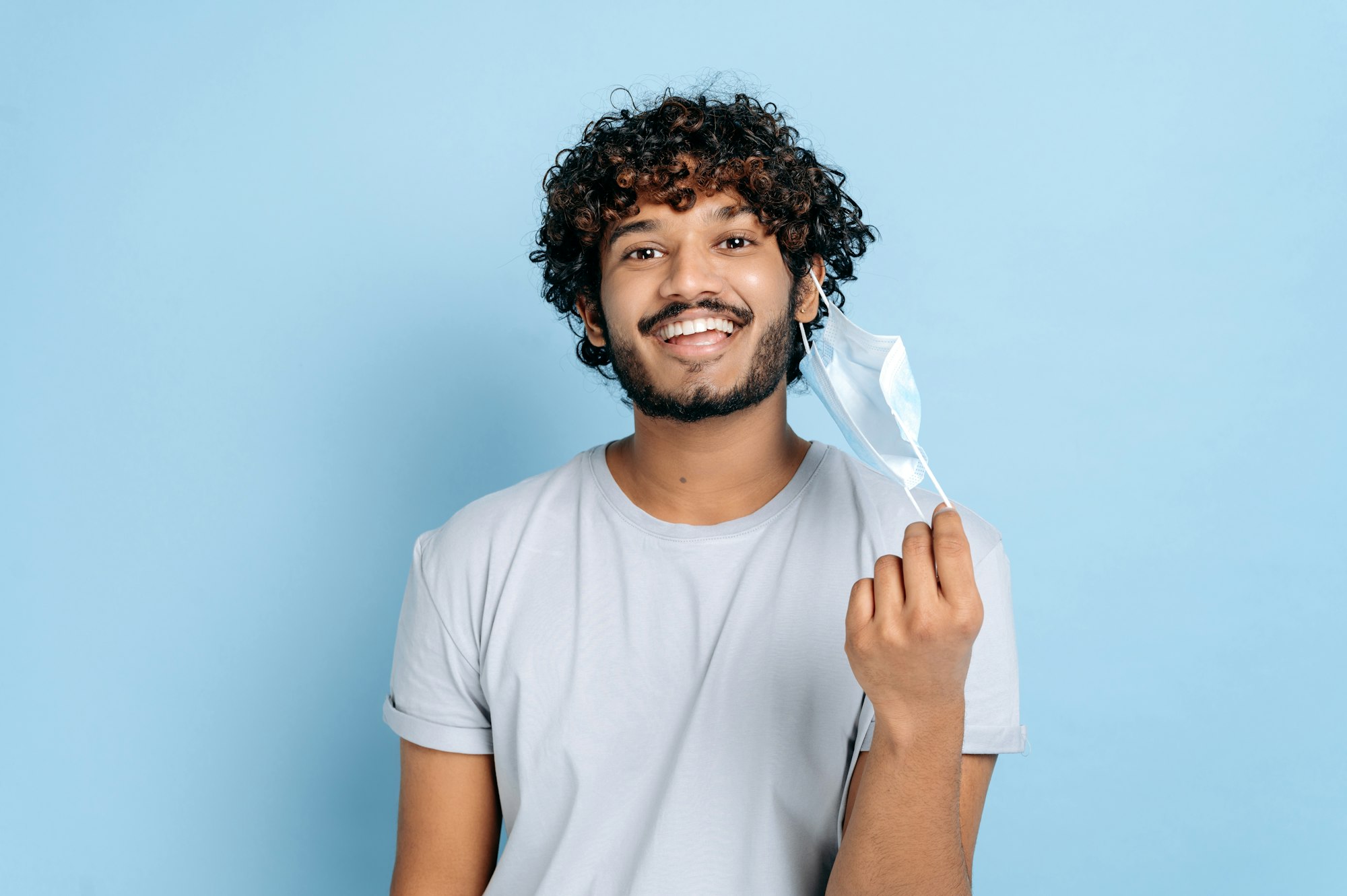 Recovery, cancellation of quarantine. Happy indian or arabian curly-haired guy, takes off protective